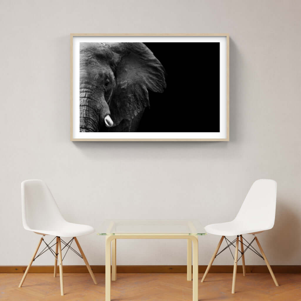 Framed elephant face print on wall above modern table and chairs, showcasing African wildlife art.