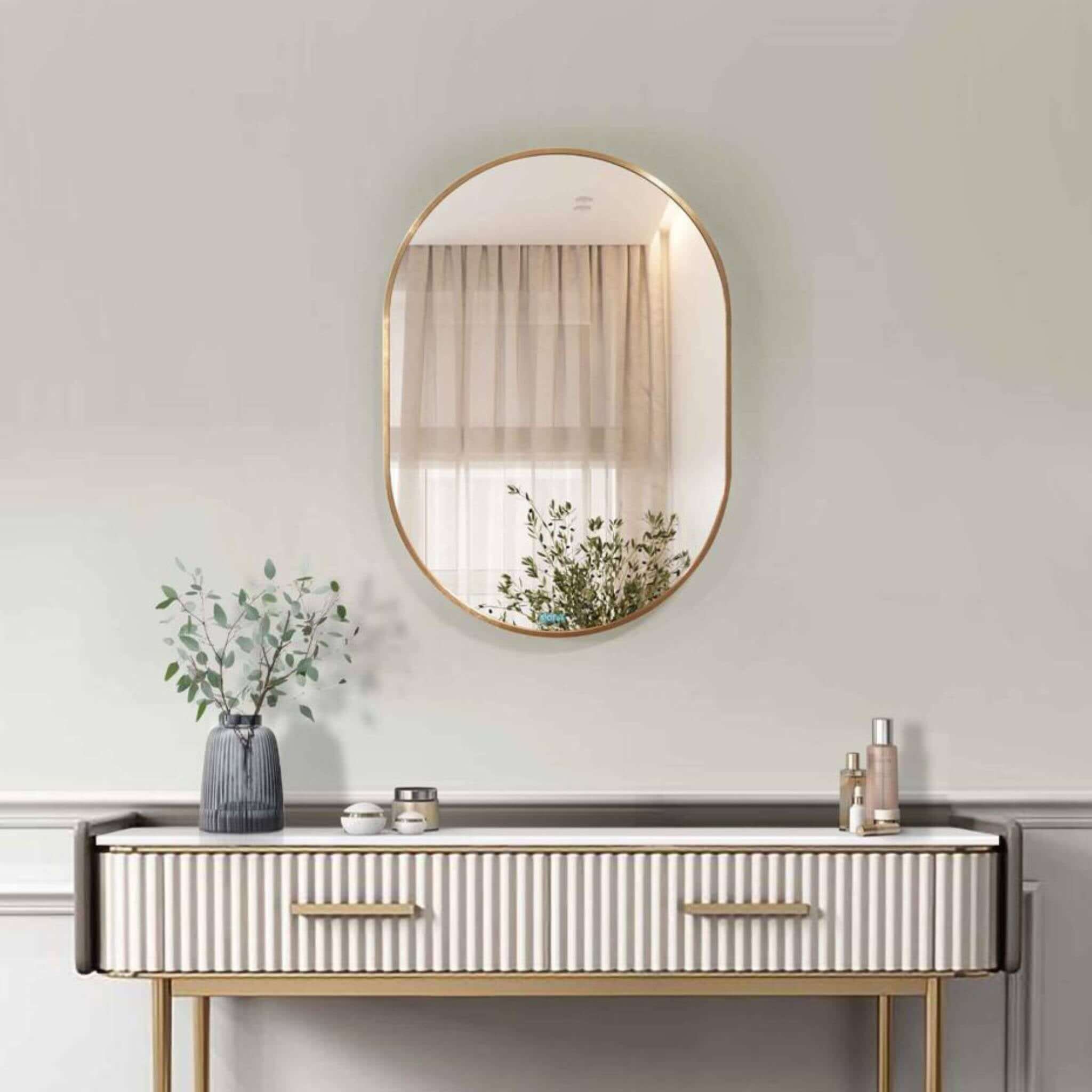 Small oval aluminium mirror with a gold frame, enhancing a modern minimalist decor setup.