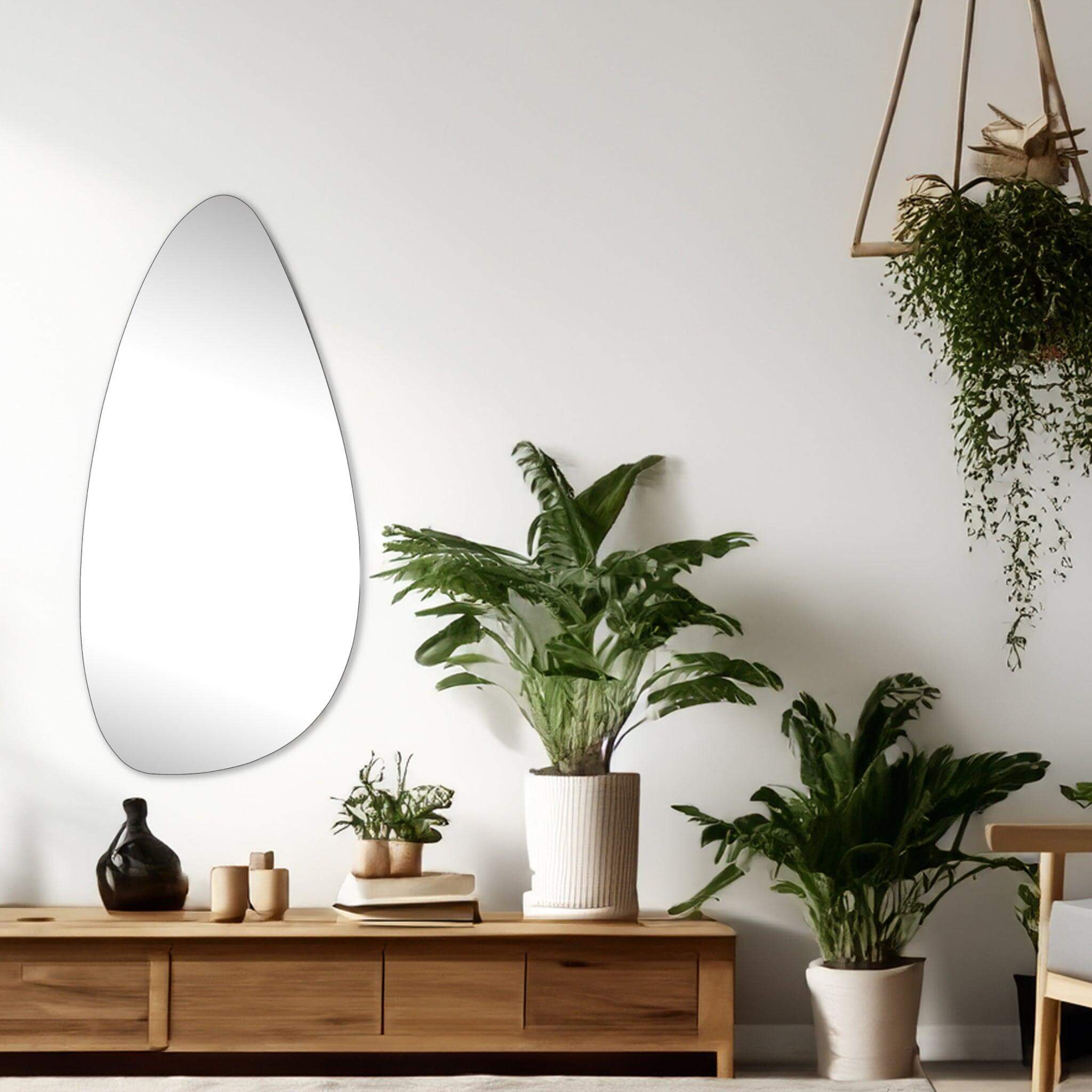 Ira Irregular Tear Drop Mirror reflecting light in a modern living room setting with indoor plants.