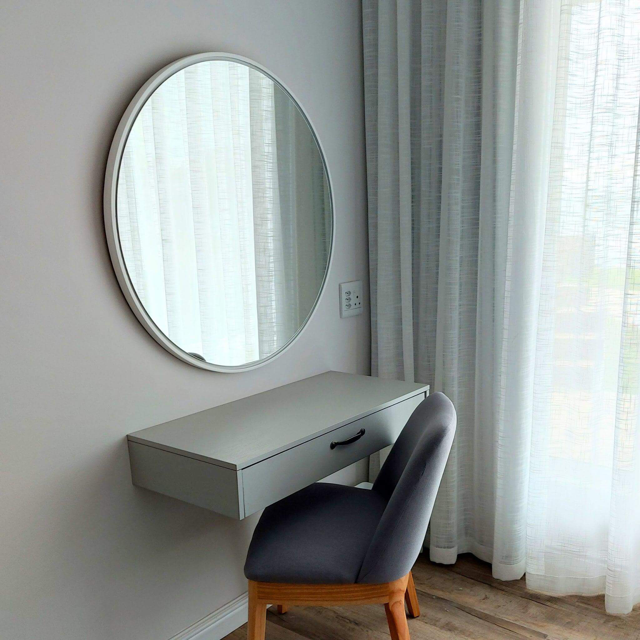 Lily Round Mirror above a modern grey desk with a stylish chair, enhancing contemporary room decor.